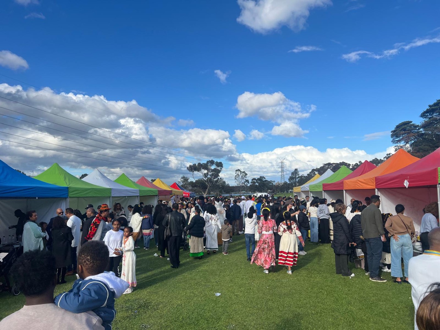 A corridor of colourful market tents at Footscray Park filled with people in traditional dress